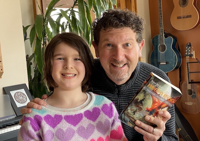 Ephie and Blue smiling, holding an advance copy of Phoenix Rising